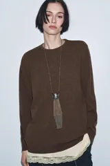 Jersey de lana color marrón con cuello redondo y manga larga. Presenta un diseño de capas con un bajo interior de encaje en color crema que simula un vestido.