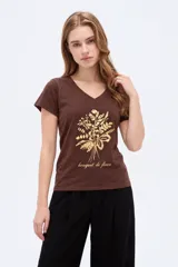 Remera marrón de algodón, con cuello en V, mangas cortas y ajuste al cuerpo. Cuenta con un estampado frontal metalizado en tono dorado de un ramo de flores y la inscripción "bouquet de fleurs".
