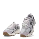 Championes New Balance 530 de estilo urbano, confeccionados en malla gris y superposiciones de gamuza en tono lila. Cuentan con detalles en negro, entresuela blanca ABZORB y suela de goma con tacos marrones.