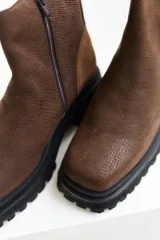 Bota corta de cuero color marrón con suela track negra y cierre lateral con cremallera.