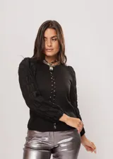 Blusa negra de tejido de punto acanalado, con cuello redondo y mangas largas abullonadas de tela semitransparente. Presenta una hilera vertical de pequeñas cuentas plateadas en el frente.