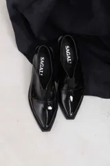 Mocasines de charol color bordó, de diseño vanguardista con corte asimétrico en el empeine, abertura en V, punta fina y suela plana con pequeño tacón.