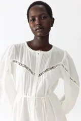 Vestido túnica corto de algodón con efecto arrugado y diseño holgado. Cuenta con inserciones de encaje, cuello redondo y cierre frontal de botones. Presenta mangas globo largas con puños elásticos, cinturón fino extraíble para ajustar la cintura y costura fruncida en el bajo con volados.