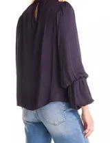 Blusa Tahari de gasa satén color violeta oscuro, con cuello alto fruncido y mangas largas abullonadas. La espalda tiene una abertura central con cierre de botón.