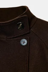 Chaqueta corta de paño en color beige, con cuello subido, manga larga y cierre frontal cruzado con botones oscuros. Presenta bolsillos delanteros de vivo.