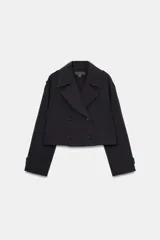 Trench corta de color negro con cuello de solapa, cierre frontal cruzado con botones y mangas largas con trabillas ajustables. Cuenta con bolsillos delanteros de vivo.