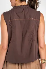 Blusa de algodón sin mangas en color blanco off-white, con cuello alto con volados y cierre frontal de cordones ajustables con lazos. Presenta detalles de encaje y bordados sutiles en la parte delantera.