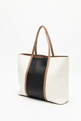 Cartera tipo tote bag en símil cuero, con diseño en bloques de color negro y blanco, y detalles en marrón. Tiene asas largas para llevar al hombro y un cierre magnético.