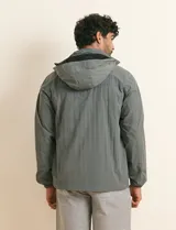 Campera impermeable gris con capucha, cierre frontal y bolsillos laterales con cremallera.