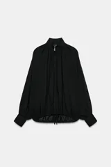 Camisa de algodón color negro, con cuello subido, manga larga terminada en puño ancho y bajo ajustable con cordones. Cuenta con cierre delantero con botones ocultos por solapa y detalles fruncidos.