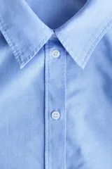 Camisa de algodón color celeste, con cuello clásico, cierre frontal de botones y mangas largas con puños sencillos. Presenta corte relajado y bajo redondeado.