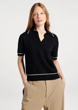 Polo de manga corta confeccionado en tejido de punto negro, con cuello tipo polo y detalles de líneas finas en color crema en el cuello, puños y ruedo.
