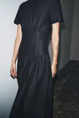 Vestido midi de denim color negro con cuello redondo y manga corta. Presenta un diseño con cintura entallada tipo bustier y falda con corte evasé. Cierre posterior con cremallera.