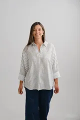 Blusa de corte oversize con estampado de rayas verticales en color verde sobre fondo blanco. Presenta cuello camisero con escote en V, mangas largas con puños anchos y un diseño holgado y fluido.