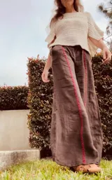 Pantalón ancho de lino color tostado, con cintura elástica y detalles de bordado rojo a lo largo de las piernas.