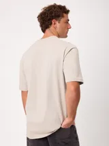 Remera holgada de algodón color beige con lavado ácido, cuello redondo ancho y diseño de tres pequeños círculos estampados en el pecho.