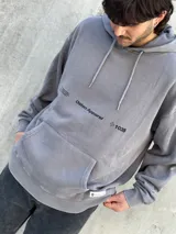 Canguro gris con capucha ajustable con cordones, bolsillo tipo canguro y logo estampado en el pecho.