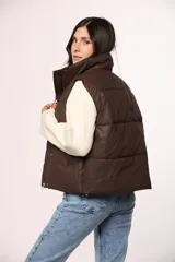 Chaleco puffer de nylon en color verde oliva, con cuello alto, cierre frontal con cremallera y botones a presión, y bolsillos laterales.