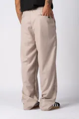 Pantalón sastrero de corte baggy, color beige, con pinzas frontales, cierre de botón y cremallera, y bolsillos laterales.