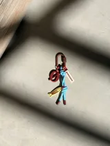 Charm para bolso con mosquetón marrón, cordón de tela celeste con nudos, dije de pez amarillo, dije circular marrón y etiqueta rectangular con la inscripción Uruguay.