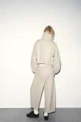 Sudadera tipo bomber de tejido suave, color beige, con cuello alto ajustable mediante cordones, cierre frontal con cremallera, mangas largas con puños elásticos y bolsillos laterales de vivo.