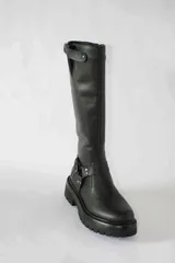 Bota de caña alta confeccionada en cuero color marrón, con suela track gruesa antideslizante. Presenta estribo decorativo con hebillas metálicas en el tobillo y detalle de ajuste con hebilla en la parte superior de la caña.