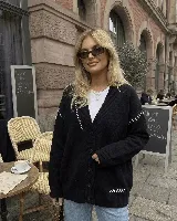 Saco oversize negro de punto, con cuello en V, cierre frontal de botones y detalles de costuras bordadas en blanco.