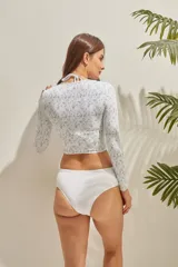 Top de bikini de manga larga con cuello redondo, diseño crop top y estampado botánico en tonos grisáceos sobre fondo blanco.