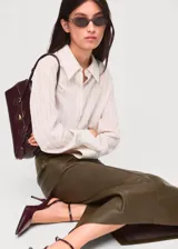 Falda midi de corte lápiz confeccionada en material efecto piel color verde oliva, con tiro medio y abertura posterior en el bajo.