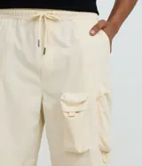 Bermuda baggy cropped de color beige, confeccionada en poliéster, con bolsillos cargo laterales y cintura elástica.