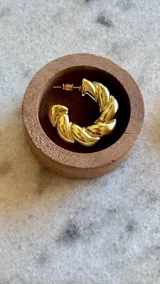 Aros tipo argolla con diseño trenzado en acabado dorado brillante.
