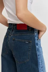 Jean wide leg de tiro medio, confeccionado en denim azul con detalles de paneles laterales en un tono más oscuro, tiro medio, cierre frontal con botón y cremallera, y diseño de perneras amplias.