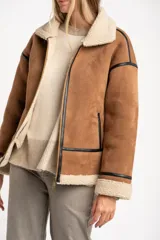 Campera tipo gamulán de corte oversize, confeccionada en material efecto gamuza color camel con interior y detalles de cuello y puños en corderito sintético color crema. Presenta cierre frontal y detalles de ribetes en cuero sintético negro.