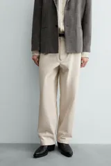 Pantalón chino de corte relajado, confeccionado en tejido estructurado de color beige. Presenta bolsillos frontales, bolsillos traseros de vivo y cierre frontal con cremallera y botón.