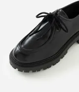 Zapato estilo desert shoe u oxford de Satinato, confeccionado en poliuretano (PU) negro con acabado texturizado. Presenta diseño de punta redonda, cordones al tono y suela gruesa tractorada de goma.