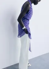 Vestido corto de poliéster con estampado de lunares, cuello en pico cruzado y diseño evasé. Presenta tirantes anchos y cierre mediante lazo lateral.