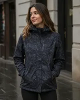 Campera cortaviento impermeable de United Uy, confeccionada en poliéster ultra liviano. Presenta un diseño con estampado botánico en tonos oscuros, capucha ajustable, cierre frontal con solapa y bolsillos laterales.