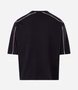 Remera masculina de corte boxy, color negro, con cuello redondo y mangas cortas amplias. Presenta detalles de vivos blancos en contraste a lo largo de las costuras de las mangas y hombros.