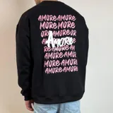 Buzo de cuello redondo y corte oversize, color blanco, con estampa gráfica en la espalda que repite la palabra 'Amore' en tonos rosados y un diseño central destacado en negro.
