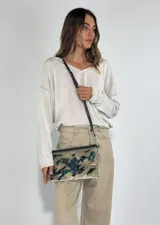 Cartera tipo sobre con lentejuelas doradas y negras reversibles, con borde superior de cuero negro y correa fina de cuero negro.