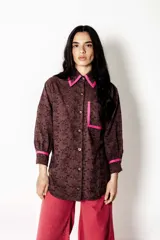 Camisa de broderie color chocolate con detalles de bies en color fucsia en el cuello, bolsillos y puños. Presenta un corte amplio, estilo relajado, mangas largas y cierre frontal con botones.