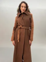 Tapado largo hasta el tobillo, confeccionado en lana merino afieltrada color marrón. Presenta un corte recto que se ajusta a la cintura con lazos. El cuello amplio y los puños largos son calados artesanalmente con un patrón de transparencia.