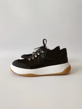 Zapatillas deportivas negras de cuero, con cordones y suela de goma blanca con base marrón.