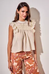 Blusa sin mangas de color crudo, con diseño oversize, cuello redondo y detalles de nido de abeja bordado en el pecho, acompañado de volados en los hombros.