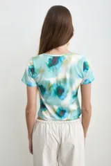 Remera de manga corta con estampado estilo acuarela en tonos de turquesa, verde y blanco, de cuello redondo y corte ajustado.
