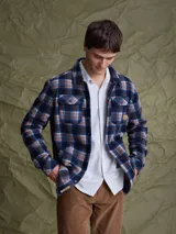 Sobrecamisa de tejido polar con estampado abstracto en tonos rojizos y azul marino. Presenta cuello clásico, cierre frontal con botones a presión, dos bolsillos frontales con solapa en el pecho y un parche decorativo.
