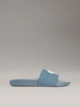Ojotas tipo slide de Calvin Klein Jeans en color azul, con logo de la marca en relieve en color verde neón sobre la banda superior y logo grabado en el lateral de la suela.