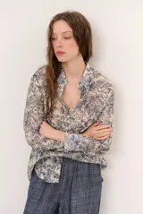 Camisa de seda color celeste y beige, con estampado de hojas en tonos azules, cuello camisero, manga larga y cierre frontal de botones.