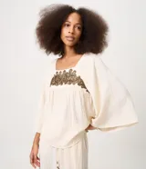Blusa tipo bata color off-white de viscosa y poliamida, con cuello redondo, mangas cortas amplias, fruncido bajo el busto y bordado delantero contrastante.