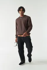 Buzo marrón de felpa con cuello redondo, mangas largas y puños acanalados. Presenta costuras a contratono, lettering estampado en el pecho, bolsillos laterales y logo en grifa de goma.